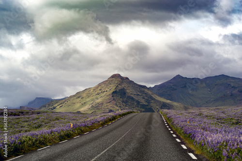 A road with colorful mountains and impressive clouds in the background
