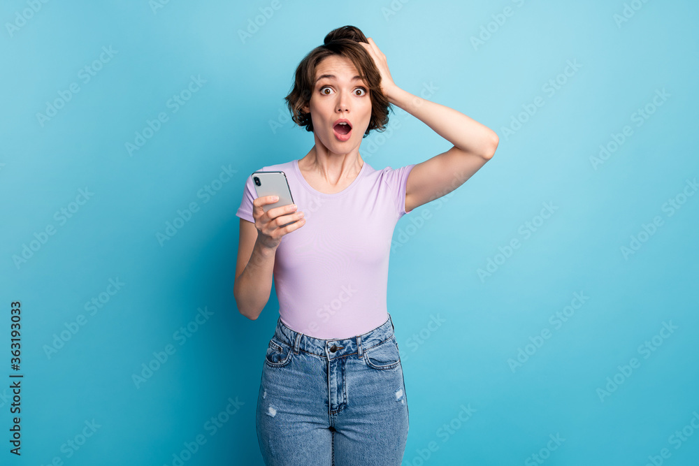 Photo of astonished addicted girl use smartphone read unbelievable social media information impressed touch hand head wear good look clothes isolated over blue color background Photo of astonished addicted girl use smartphone read unbelievable social media information impressed touch hand head wear good look clothes isolated over blue color background