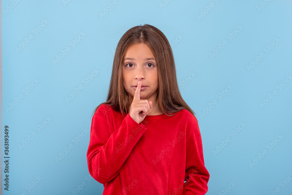 Young girl asks not to tell a secret, isolated on blue background with copy space in studio. Young girl asks not to tell a secret, isolated on blue background with copy space in studio.