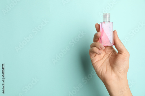 Woman holding antiseptic gel on light blue background, closeup. Space for text