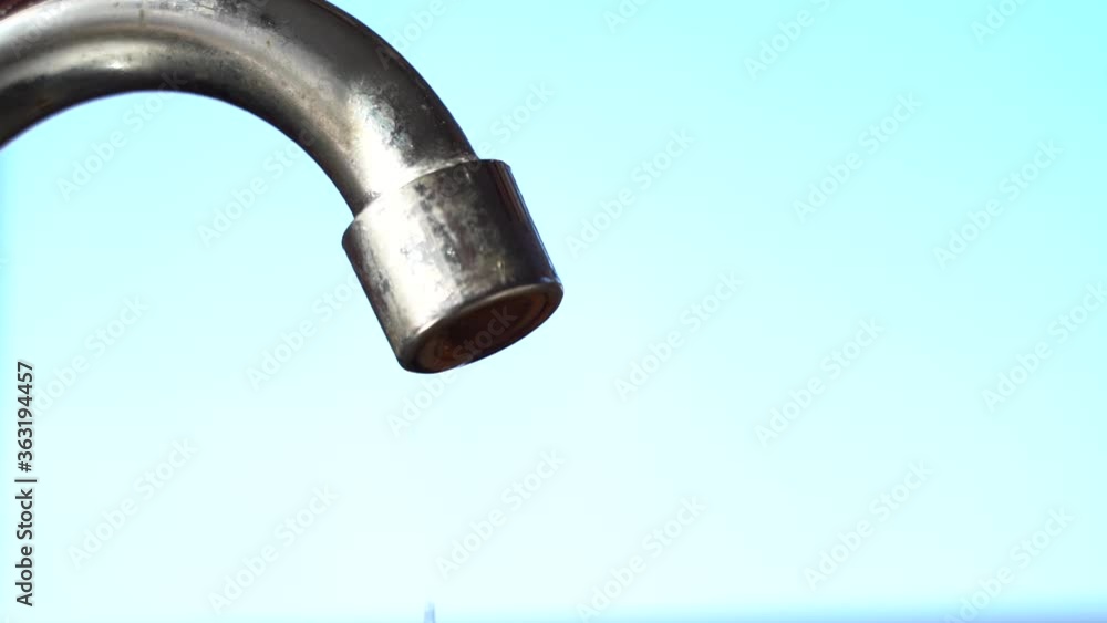 Dripping water from a tap on a sky blue background. Macro shot. Natural daylight. Chrome water tap. Dripping water from a tap on a sky blue background. Macro shot. Natural daylight. Chrome water tap.