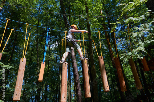 A boy with a helmet and insurance passes a high-altitude obstacle course.