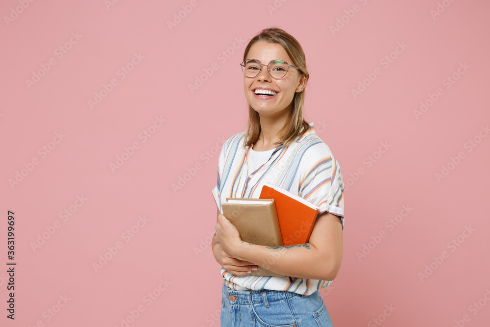 Cheerful young student girl in casual striped shirt eyeglasses posing isolated on pink background studio portrait. Education in high school university college concept. Mock up copy space. Hold books. Cheerful young student girl in casual striped shirt eyeglasses posing isolated on pink background studio portrait. Education in high school university college concept. Mock up copy space. Hold books.