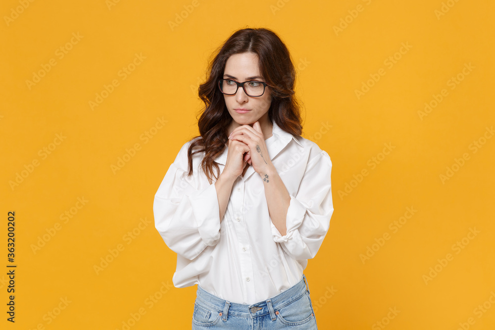 Pensive young brunette business woman in white shirt glasses isolated on yellow background studio portrait. Achievement career wealth business concept. Mock up copy space. Put hands prop up on chin.