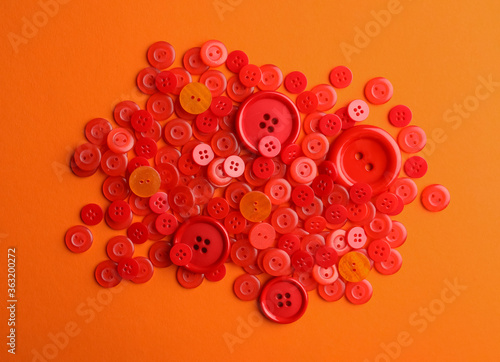 Many red sewing buttons on orange background, flat lay
