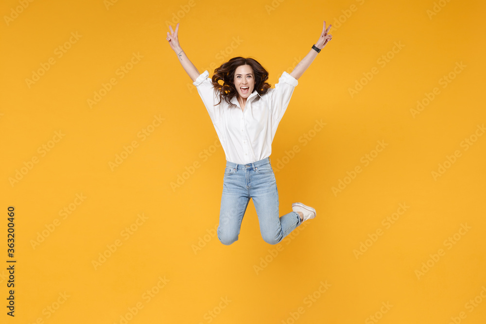 Funny young brunette business woman in white shirt posing isolated on yellow background studio portrait. Achievement career wealth business concept. Mock up copy space. Jumping, showing victory sign. Funny young brunette business woman in white shirt posing isolated on yellow background studio portrait. Achievement career wealth business concept. Mock up copy space. Jumping, showing victory sign.