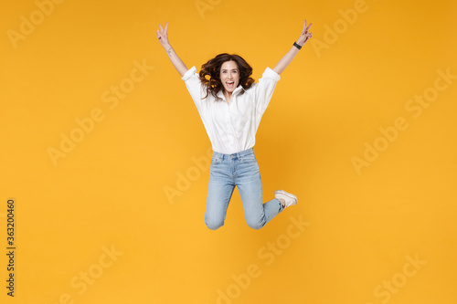 Funny young brunette business woman in white shirt posing isolated on yellow background studio portrait. Achievement career wealth business concept. Mock up copy space. Jumping, showing victory sign.