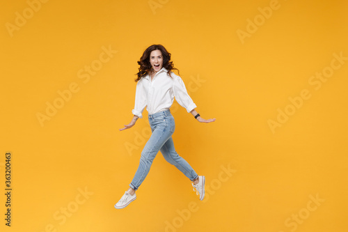 Excited young brunette business woman in white shirt posing isolated on yellow background in studio. Achievement career wealth business concept. Mock up copy space. Jumping, spreading hands and legs.
