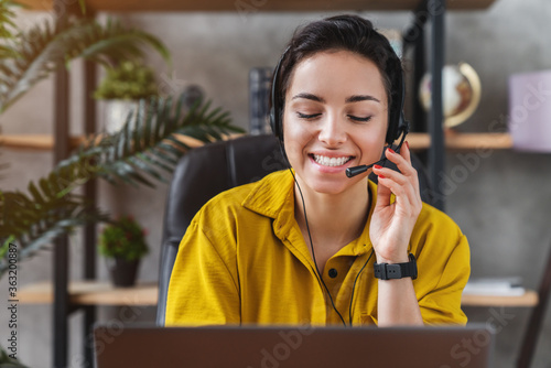 Smiling young female teleoperator working in home office with laptop and headset on photo