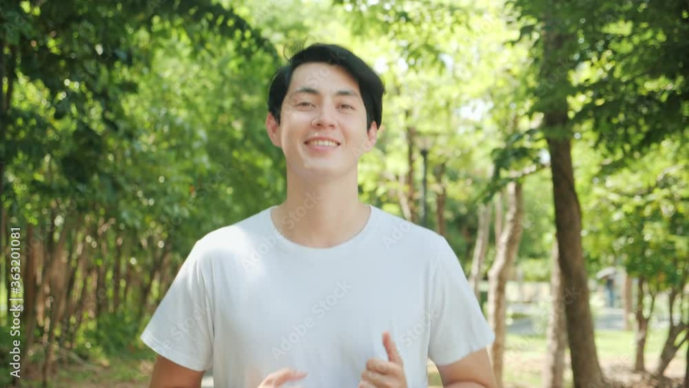 Happy handsome Asian man running in park on public green background, Fit man jogging at outdoor workout on background of trees. Healthy lifestyle concept. Slow motion Happy handsome Asian man running in park on public green background, Fit man jogging at outdoor workout on background of trees. Healthy lifestyle concept. Slow motion