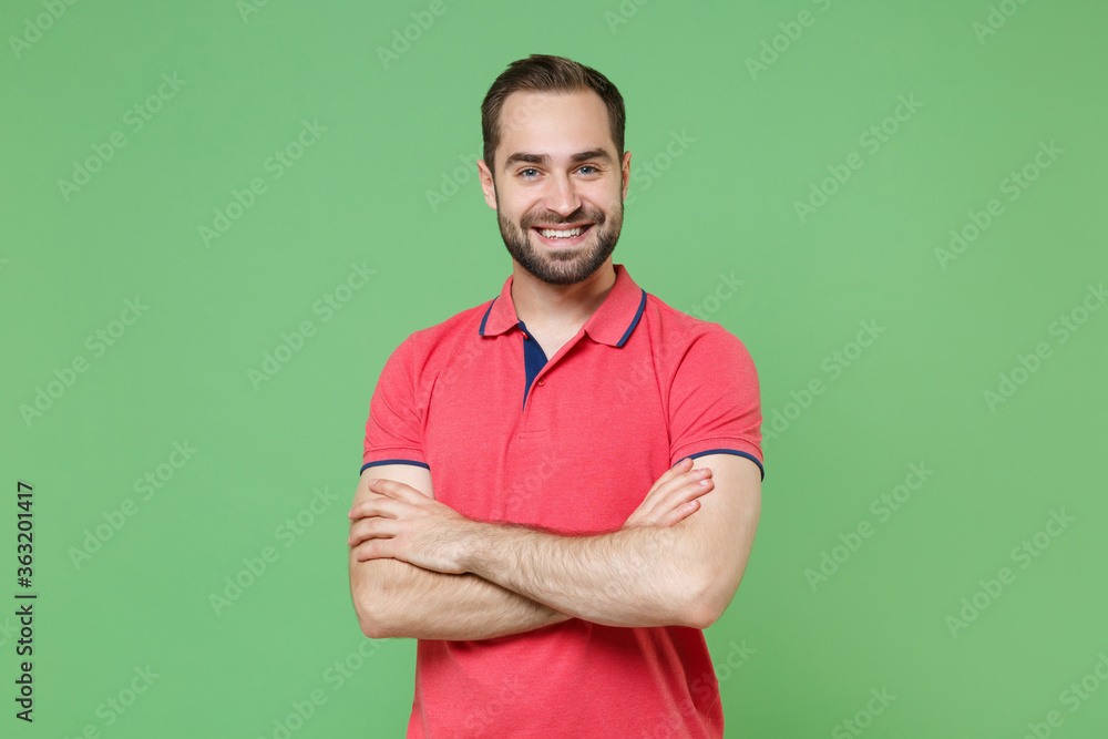 Smiling young bearded man guy in casual red pink t-shirt posing isolated on green wall background studio portrait. People sincere emotions lifestyle concept. Mock up copy space. Holding hands crossed. Smiling young bearded man guy in casual red pink t-shirt posing isolated on green wall background studio portrait. People sincere emotions lifestyle concept. Mock up copy space. Holding hands crossed.