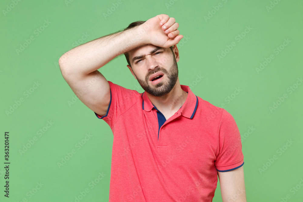 Exhausted tired young bearded man guy in casual red pink t-shirt posing isolated on green background studio portrait. People lifestyle concept. Mock up copy space. Put hands on head, having headache. Exhausted tired young bearded man guy in casual red pink t-shirt posing isolated on green background studio portrait. People lifestyle concept. Mock up copy space. Put hands on head, having headache.
