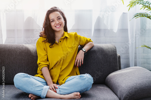 Smiling young woman relaxing while sitting on comfortable couch in living room photo