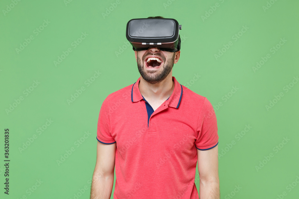 Screaming young bearded man guy in casual red pink t-shirt posing isolated on green wall background studio portrait. People sincere emotions lifestyle concept. Mock up copy space. Watching in headset. Screaming young bearded man guy in casual red pink t-shirt posing isolated on green wall background studio portrait. People sincere emotions lifestyle concept. Mock up copy space. Watching in headset.