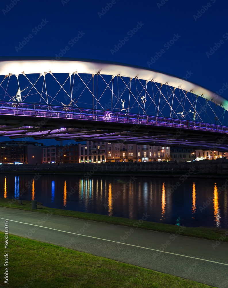 Obraz premium Father Bernatek footbridge lit up at night with reflections in the river - Krakow, Poland