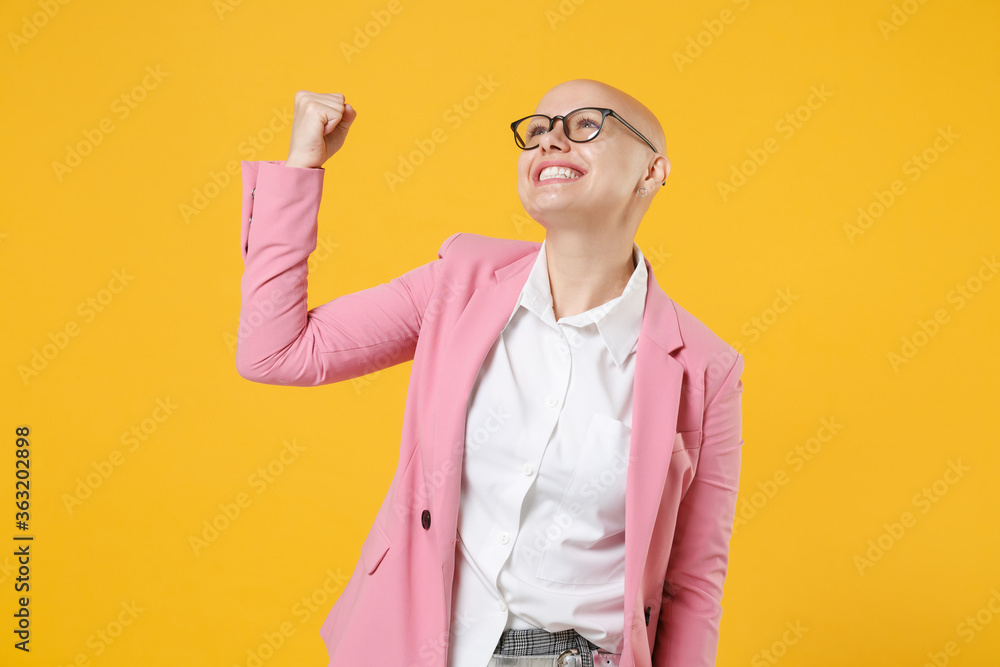 Happy young bald business woman in white shirt pink jacket glasses isolated on yellow background studio. Achievement career wealth business concept. Mock up copy space. Clenching fist like winner. Happy young bald business woman in white shirt pink jacket glasses isolated on yellow background studio. Achievement career wealth business concept. Mock up copy space. Clenching fist like winner.