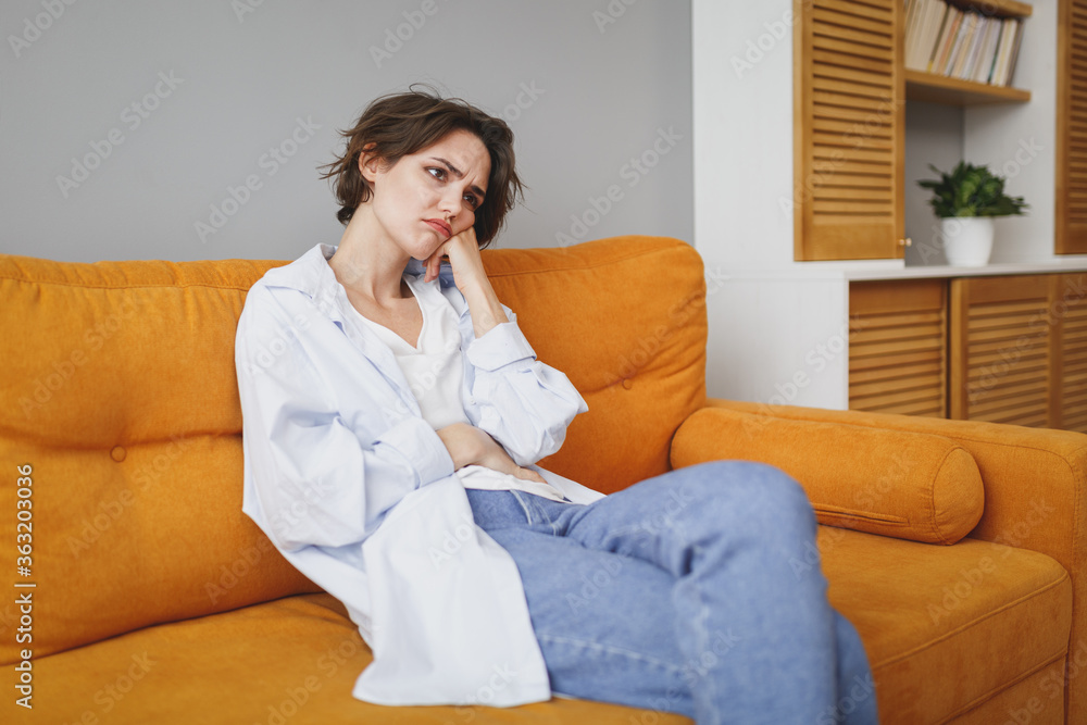 Displeased boring young brunette woman in casual clothes sitting on couch spending time in living room at home. Rest relax good mood leisure lifestyle concept. Mock up copy space. Put hand on cheek. Displeased boring young brunette woman in casual clothes sitting on couch spending time in living room at home. Rest relax good mood leisure lifestyle concept. Mock up copy space. Put hand on cheek.