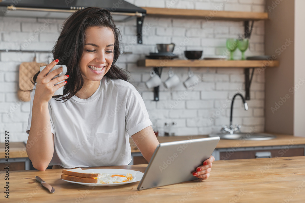 Young beautiful woman using digital tablet while healthy breakfast in modern kitchen