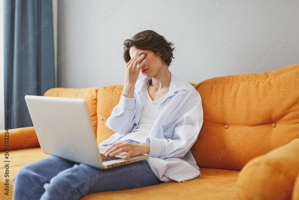 Tired exhausted young woman girl in casual clothes sitting on couch spending time in living room at home. Rest relax good mood leisure lifestyle concept. Work on laptop pc computer, put hand on head. Tired exhausted young woman girl in casual clothes sitting on couch spending time in living room at home. Rest relax good mood leisure lifestyle concept. Work on laptop pc computer, put hand on head.