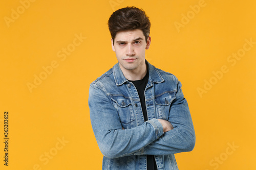Handsome young man guy 20s in casual denim jacket posing isolated on yellow wall background studio portrait. People sincere emotions lifestyle concept. Mock up copy space. Holding hands crossed. © ViDi Studio