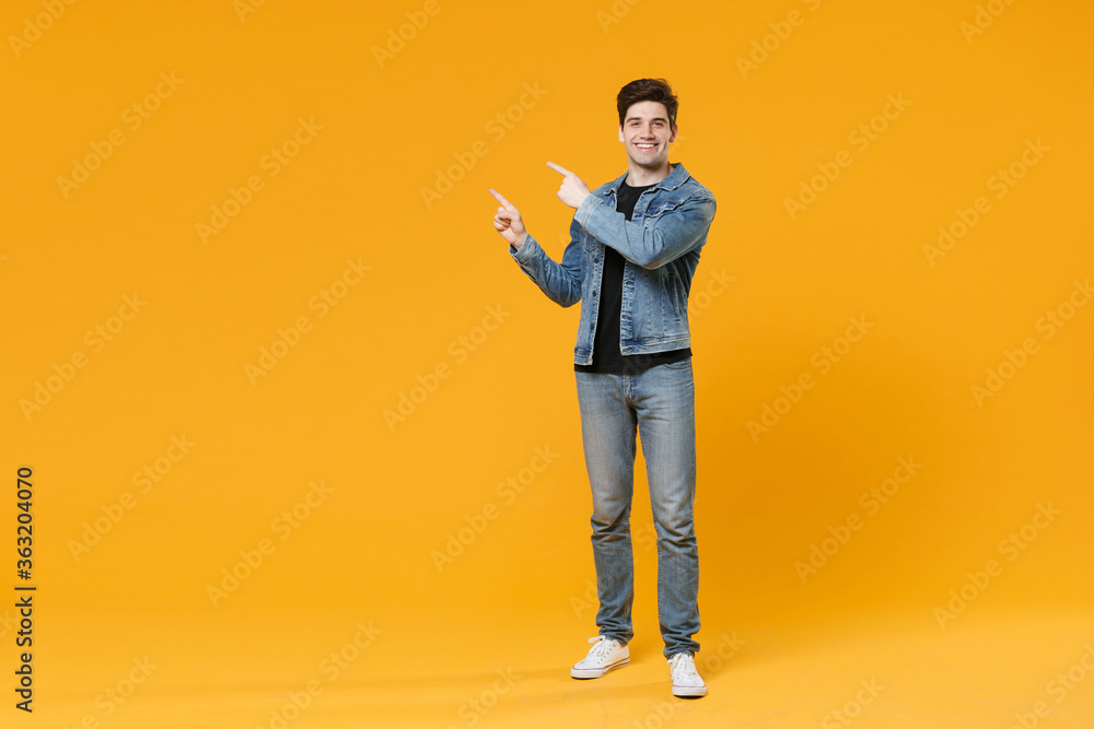 Smiling young man guy wearing casual denim clothes posing isolated on yellow background studio portrait. People sincere emotions lifestyle concept. Mock up copy space. Pointing index fingers aside up. Smiling young man guy wearing casual denim clothes posing isolated on yellow background studio portrait. People sincere emotions lifestyle concept. Mock up copy space. Pointing index fingers aside up.
