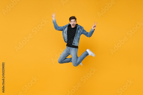 Screaming young man guy wearing casual denim clothes posing isolated on yellow background studio portrait. People sincere emotions lifestyle concept. Mock up copy space. Jumping  showing victory sign.