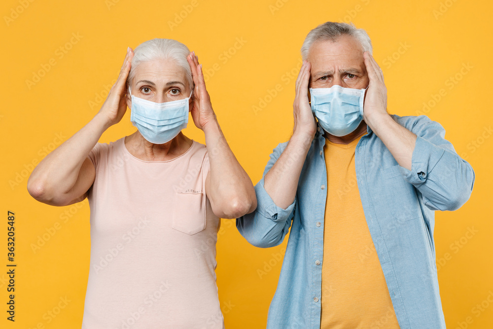 Elderly gray-haired couple woman man in casual clothes sterile face mask isolated on yellow wall background. Epidemic pandemic coronavirus 2019-ncov sars covid-19 flu virus concept. Put hands on head.