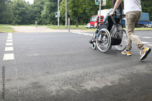 Man rolls woman in wheelchair across the road. Common areas for disabled people concept photo