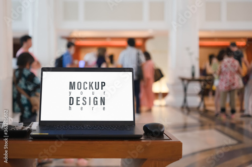 Mockup blank white screen laptop with blurred people waiting for registration in hotel hall photo