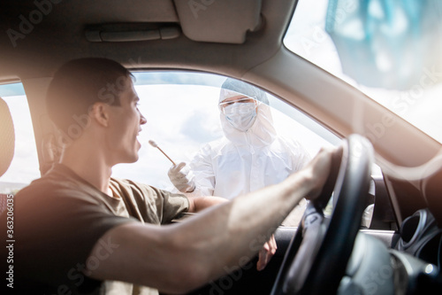 Doctor in protective virus suit taking swab from person driver to test for COVID-19 coronavirus infection