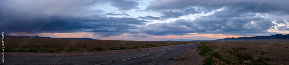 Panoramic landscape of Kazakhstan steppe in evening time with rain clouds. Clouds background. Beautiful natural wallpaper.  Scenic travel background. Travel in Kazakhstan.