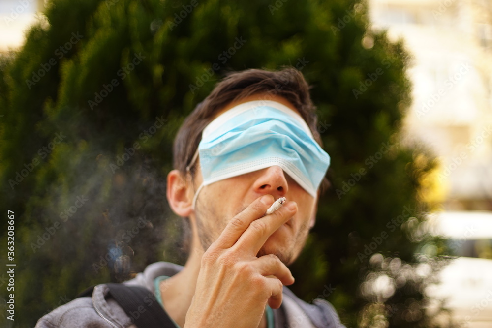 A portrait of a man with a face mask on his eyes. He is smoking a cigarette. A portrait of a man with a face mask on his eyes. He is smoking a cigarette.