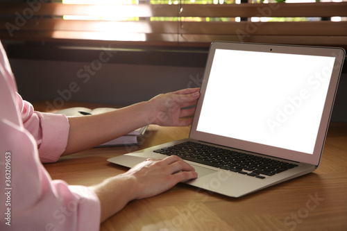 Woman using modern laptop at wooden table indoors, closeup