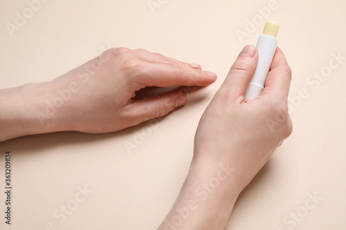 Woman holding hygienic lipstick on beige background, closeup