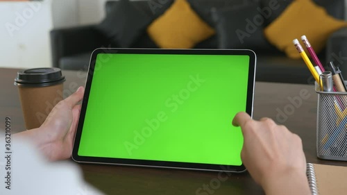 Woman holding digital tablet with green screen and touch device browsing Internet on office desk.