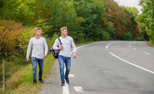 hitch hiking on empty road. travelling by hitchhiking. road trip. wanderlust concept. Hiking with friends is cool. gone to find themselves. Travel and hitch-hiking. twins walking along road