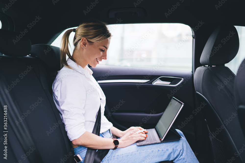 Side view of skilled female freelancer sitting at commuter seat in automobile car and using 4g wireless internet for working remotely and develop startup project, happy businesswoman typing text