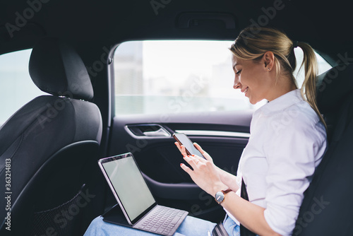 Smiling woman with smartphone sitting on back car seat