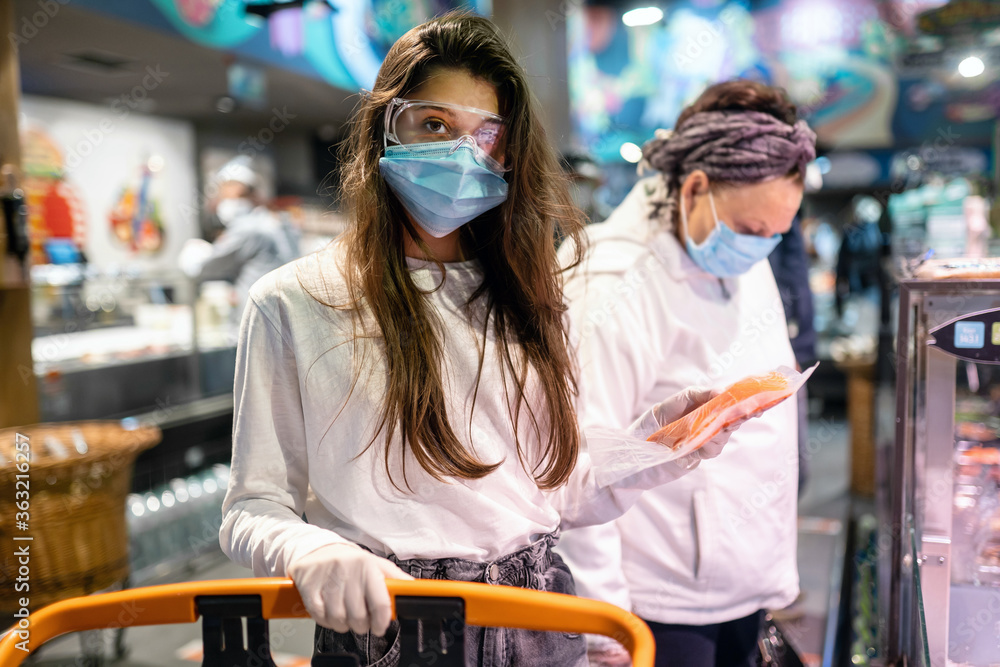 Woman with the surgical mask and the gloves is shopping in the supermarket