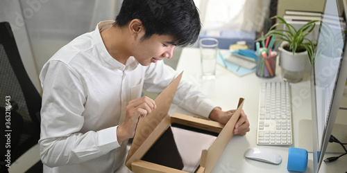 A smart man is unboxing a cardboard box from shopping online at the white working desk. photo