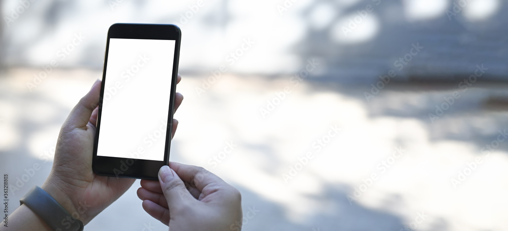 Cropped image of hands is using a white blank screen smartphone at the outdoors.