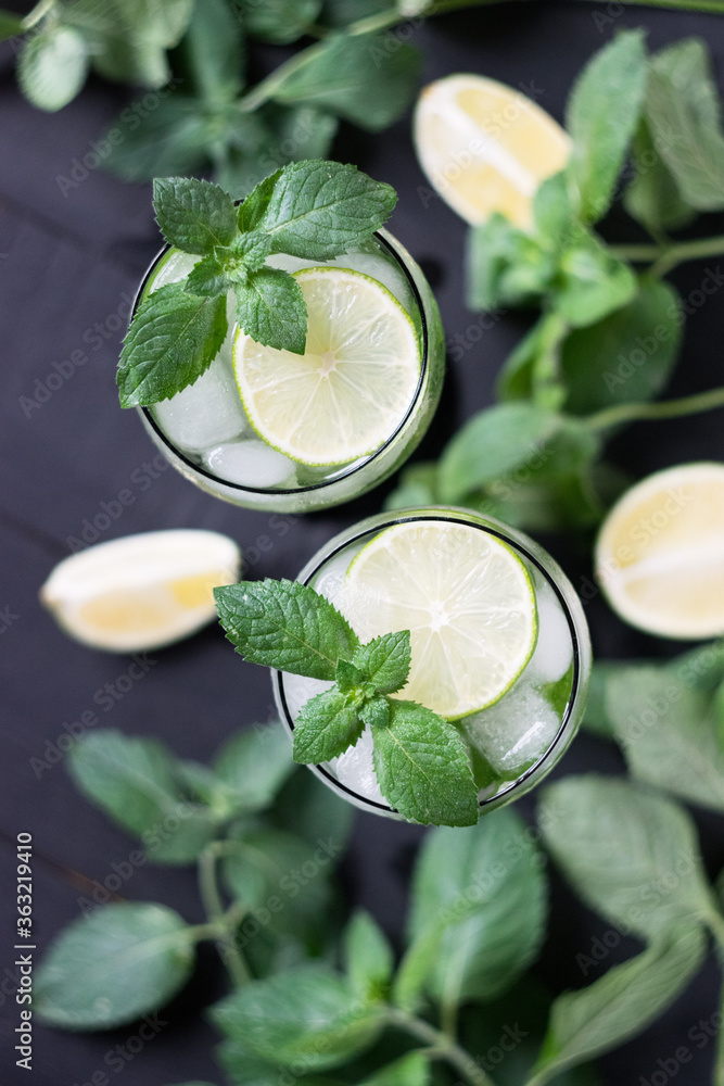 Two glasses of homemade citrus lemonade mojito with slices of lime, mint and ice on a dark wooden background.Top view. Two glasses of homemade citrus lemonade mojito with slices of lime, mint and ice on a dark wooden background.Top view.