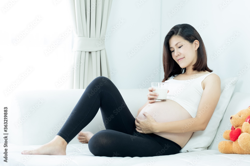 Beautiful asian pregnant woman holding a glass of milk and touching her belly Beautiful asian pregnant woman holding a glass of milk and touching her belly
