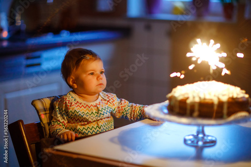 Cute beautiful little baby girl celebrating first birthday. Child blowing one candle on homemade baked cake, indoor. Birthday family party for lovely toddler child, beautiful daughter