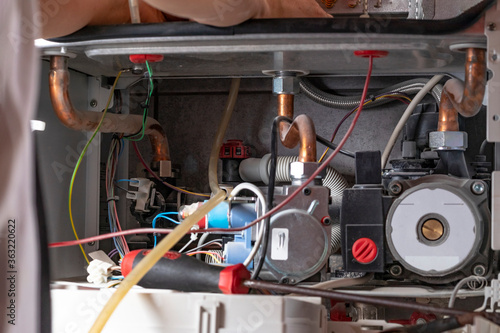 The master sets up a gas boiler, which weighs on the wall. The front dashboard is open. Using a brush and an industrial vacuum cleaner, cleaning from dirt and dirt.