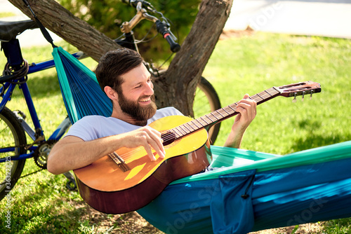Happy young man plays the guitar in a hammock on vacation.