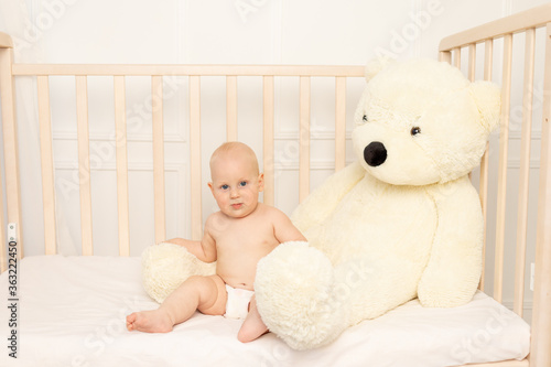 Wallpaper Mural baby boy 8 months old sitting in diapers in a crib with a large Teddy bear in the nursery, place for text Torontodigital.ca