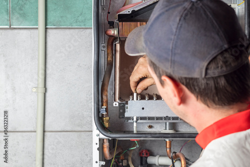 The master sets up a gas boiler, which weighs on the wall. The front dashboard is open. The removal and installation of gas nozzles for gas supply
