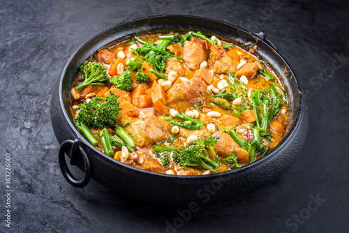 Modern style African crocodile cheeks curry with sweet potato, broccoli and peanuts as close-up in a modern design cast iron pot