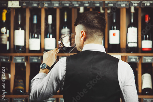 Male sommelier tasting red wine at cellar.
